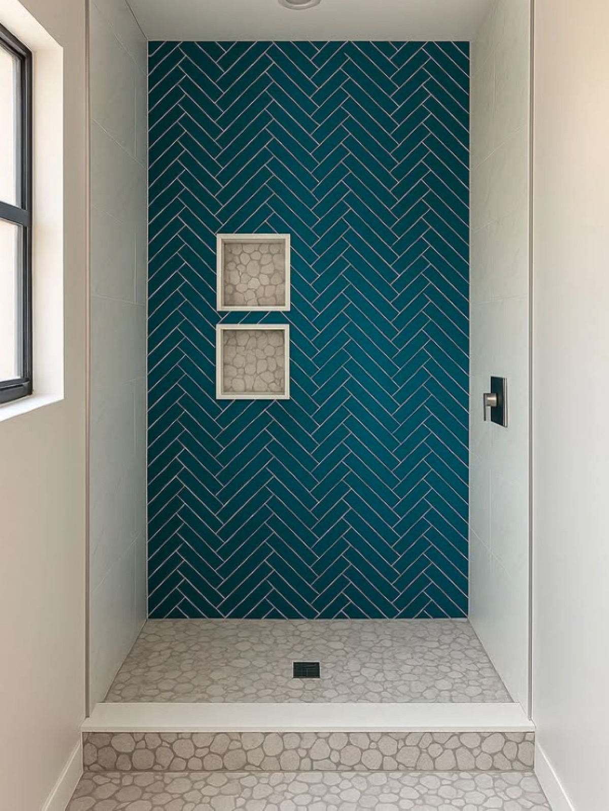 Walk-in shower with a dark teal herringbone tile feature wall, pebble mosaic niches and pebble floor