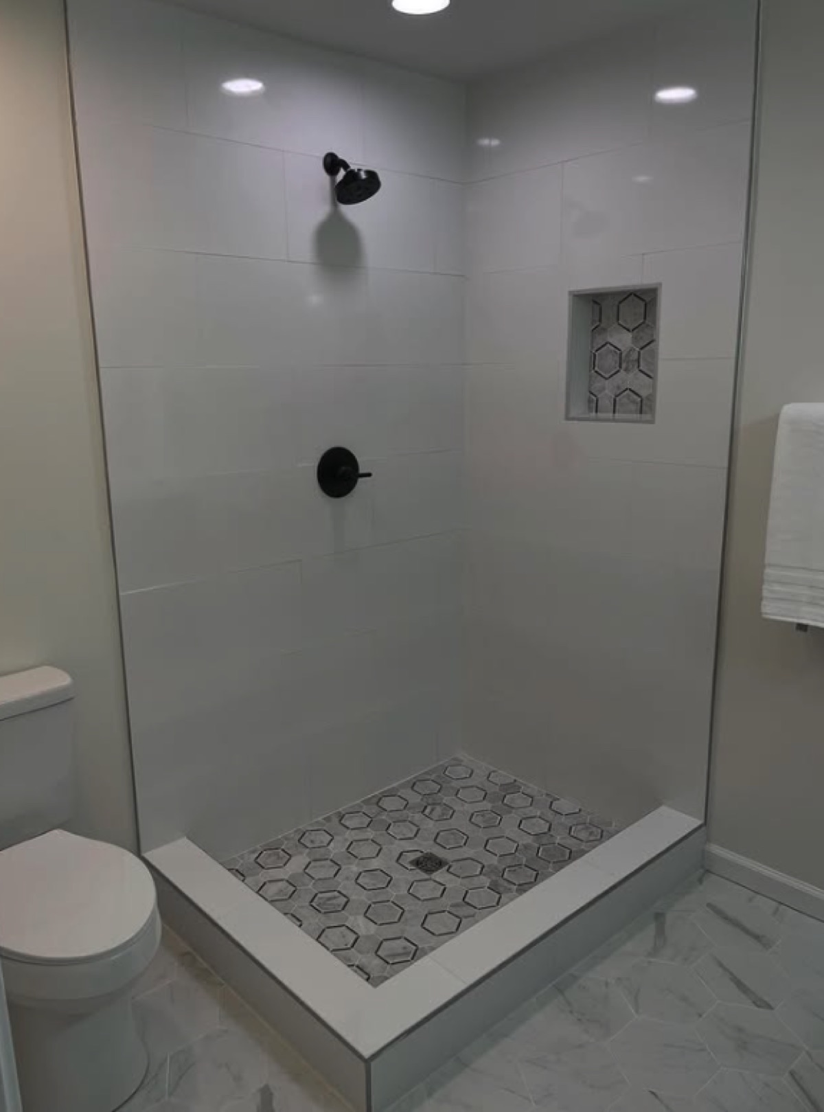 Walk-in shower with white large-format tile, grey hexagonal mosaic floor and a mosaic-lined niche