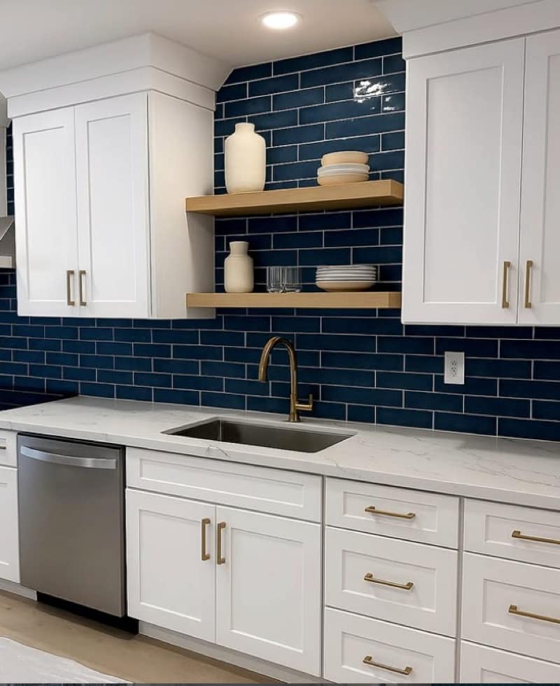Kitchen with a navy subway-tile backsplash, white Shaker cabinets, marble counters and gold fixtures