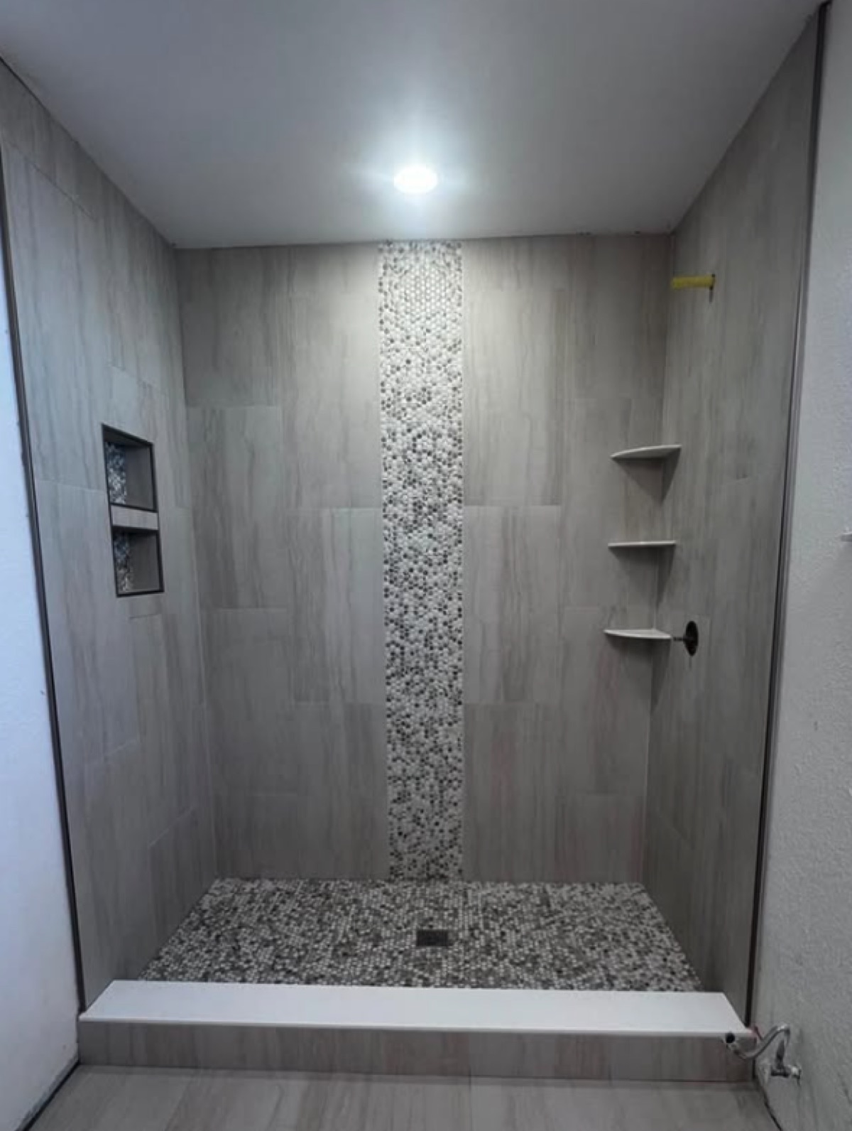 Walk-in shower with greige vertical tile, a central pebble mosaic strip and a tall pebble-lined niche