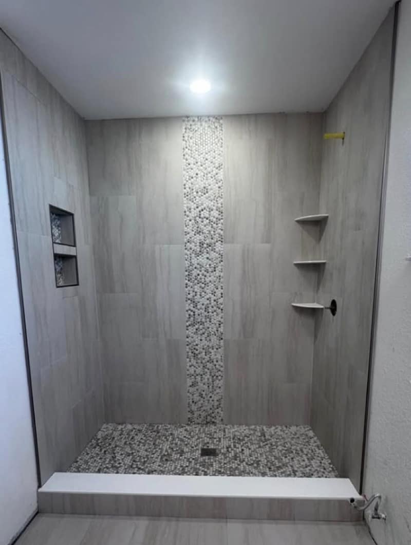 Walk-in shower with greige vertical tile, a central pebble mosaic strip and a tall pebble-lined niche