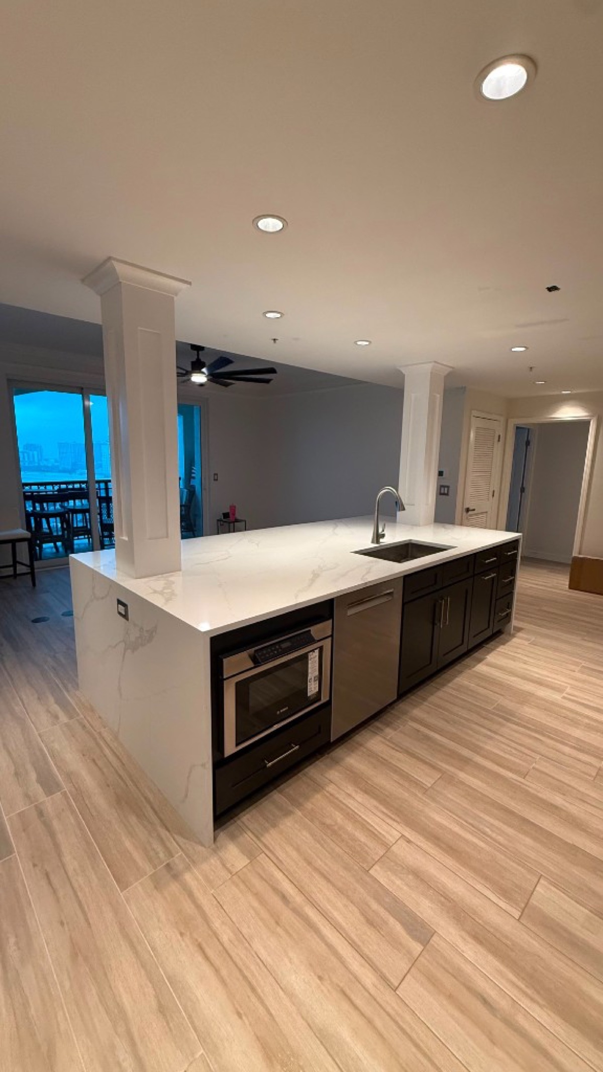 Long kitchen island with a white marble waterfall counter, dark base cabinets, stainless appliances and wood-look floor tile