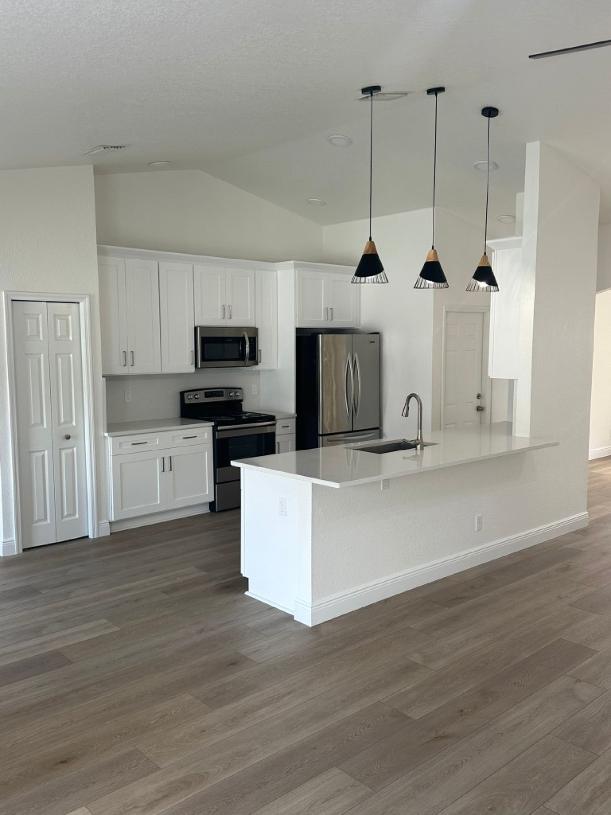 Open kitchen with white Shaker cabinets, a quartz island with a nickel faucet, stainless appliances and wood-look plank flooring