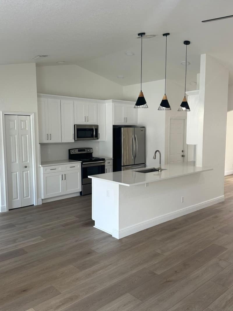 Open kitchen with white Shaker cabinets, a quartz island with a nickel faucet, stainless appliances and wood-look plank flooring